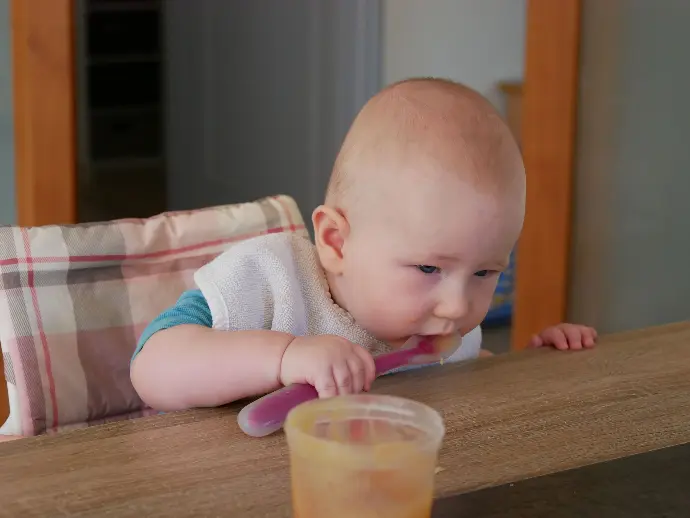 bébé de mois qui mange seul de la compote a la cuillère