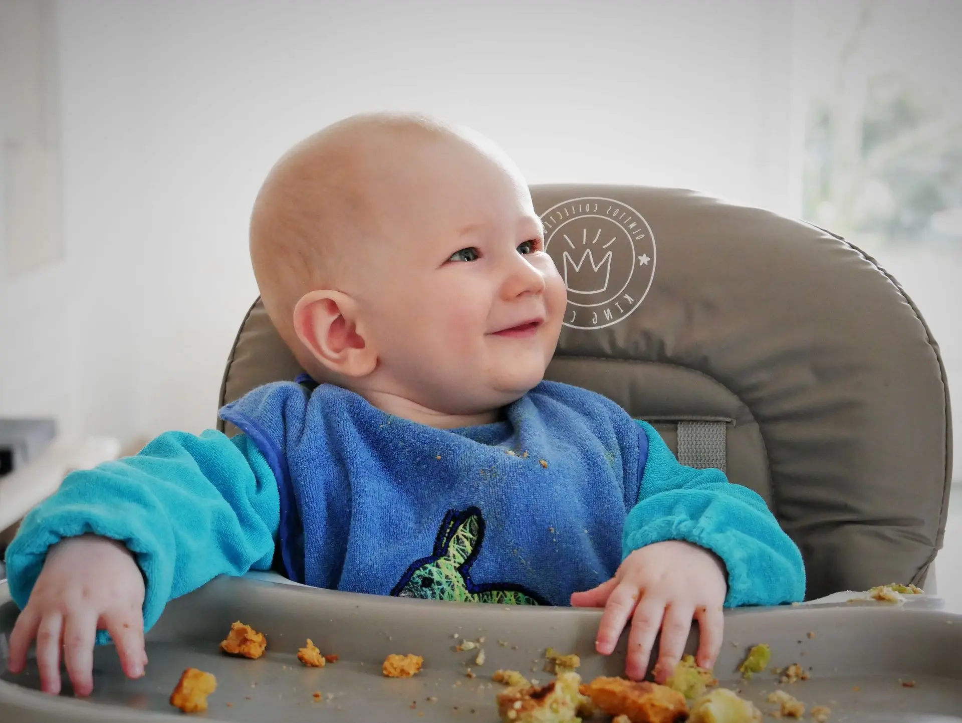 bébé souriant sur sa chaise de repas avec des bout de courge devant lui