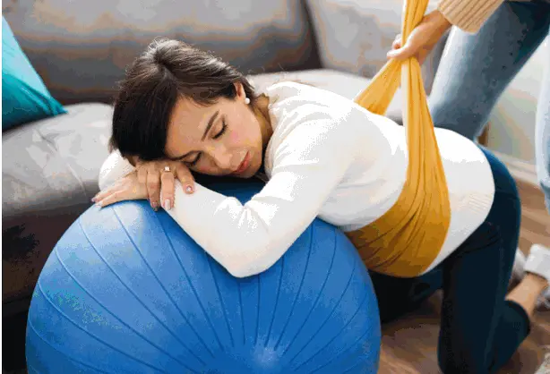 femme en appuis sur un gros ballon le ventre soutenu par un rebozo tenue dans son dos par une autre personne