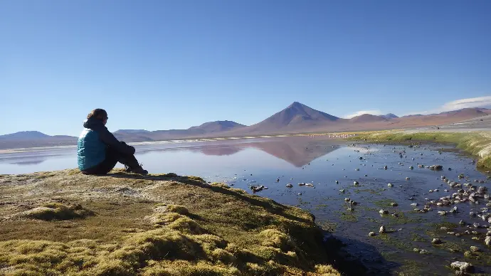 beau paysage avec un volcan un lac des reflets et de belles couleurs une femme assise sur un rocher qui regarde l'horizon